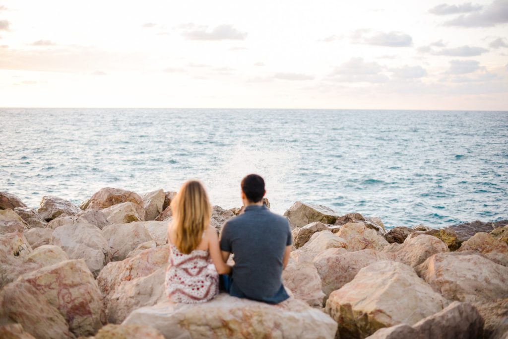 couple sitting on rocky beach facing water