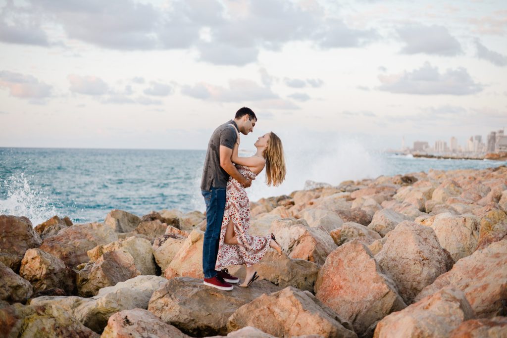 embracing man and woman posing on rocky beach for a couples photoshoot