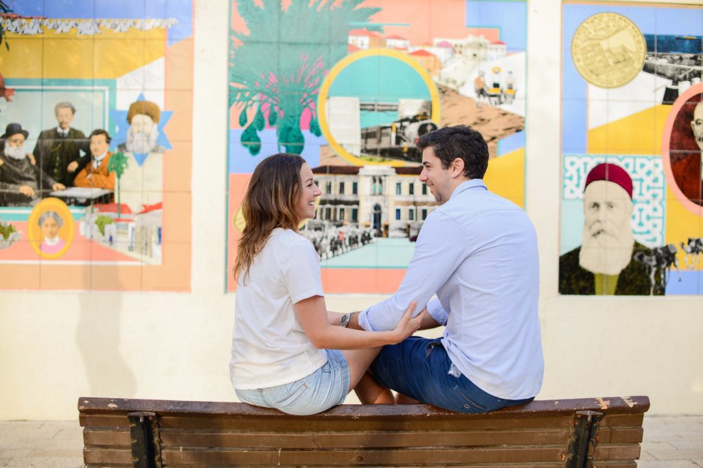 couple sitting on bench in front of mosaic wall in Neve Tzedek