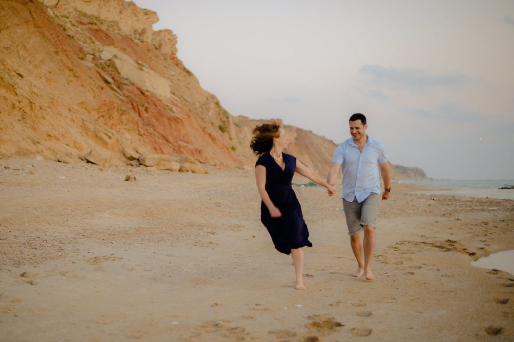 laughing couple running down beach in beach engagement photoshoot