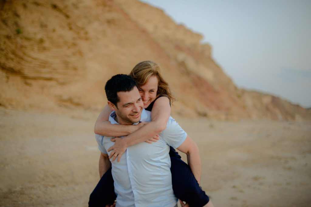 man giving woman piggy back ride in beach engagement photoshoot