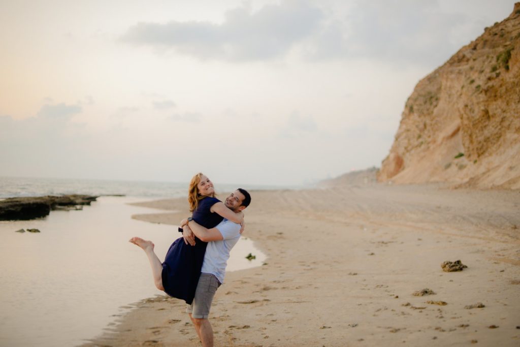 man picking up woman in beach engagement photoshoot