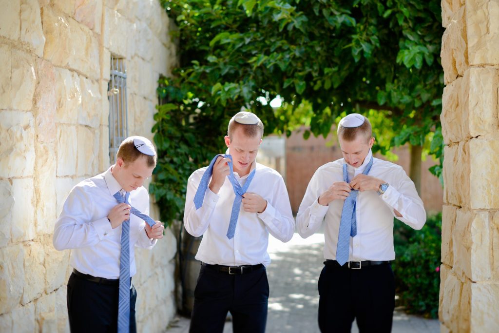 three men in groomsmen outfits fixing their ties 