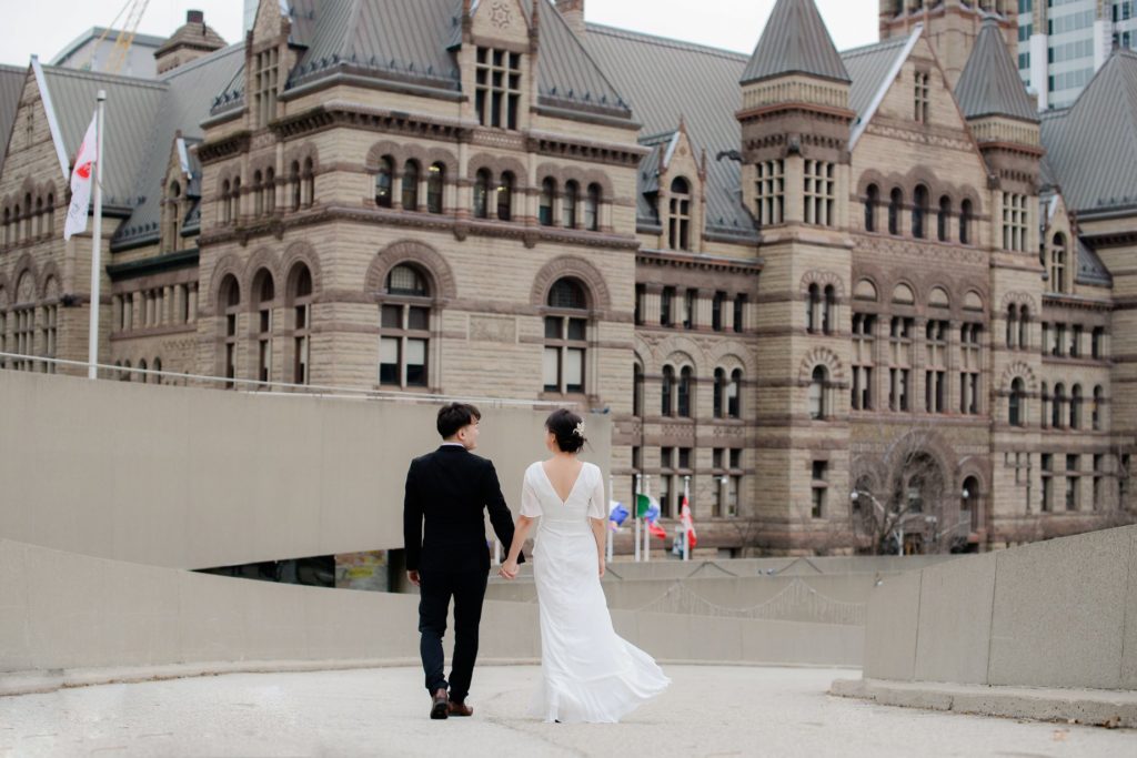 bride and groom holding hands facing toronto city hall for a wedding photoshoot