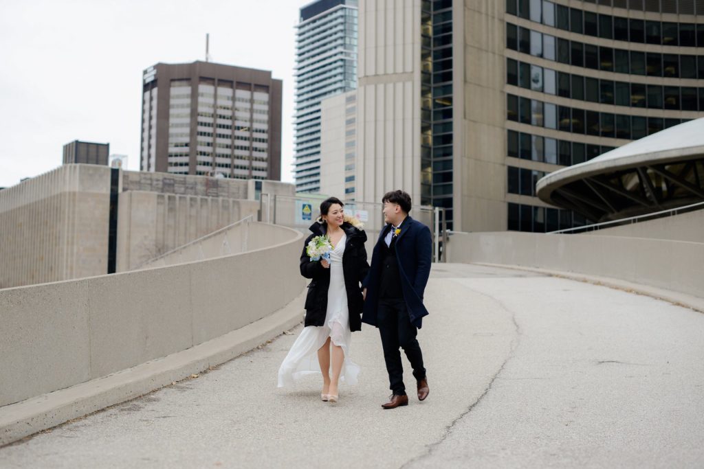 bride and groom in winter clothes walking down toronto's city hall