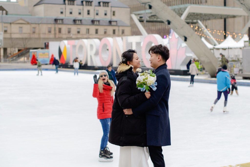 bride and groom in winter jackets posing on skate rink