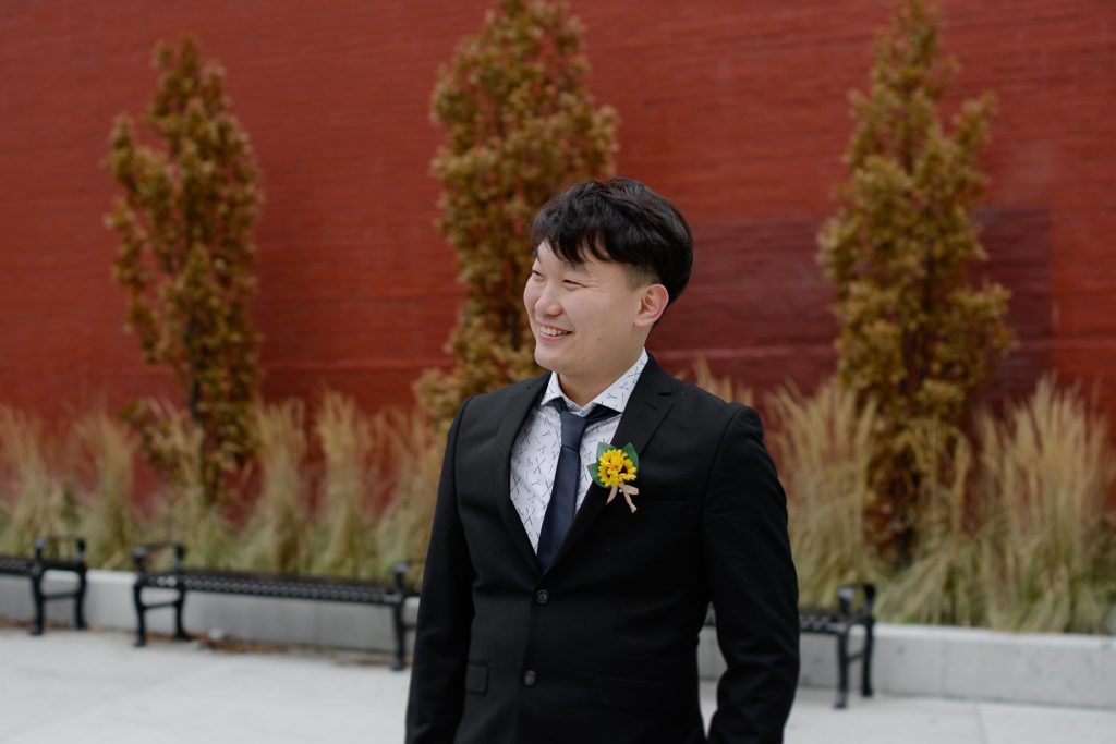 smiling groom in tuxedo against red brick wall