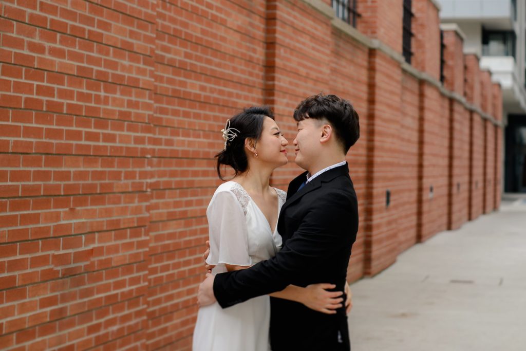 hugging couple in front of red brick wall at toronto's city hall wedding ceremony photoshoot