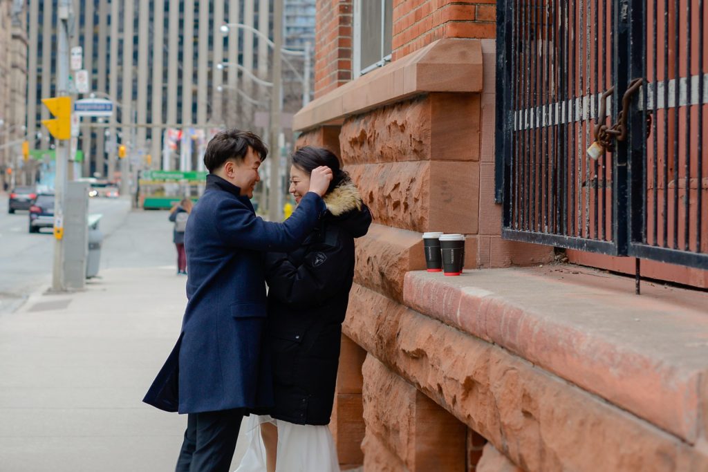 bride and groom leaning against red brick wall in the street