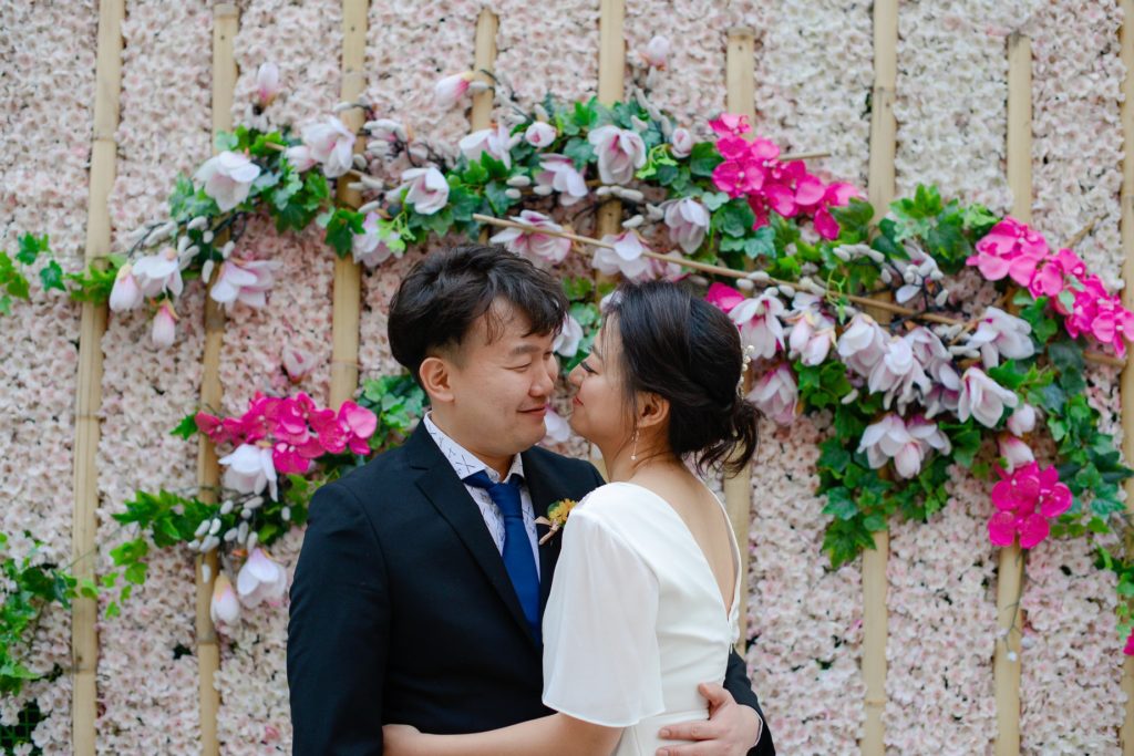 bride and room hugging in front of floral background for wedding photoshoot