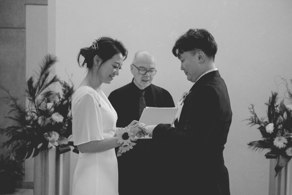 black and white photo of bride putting ring on groom's hand 