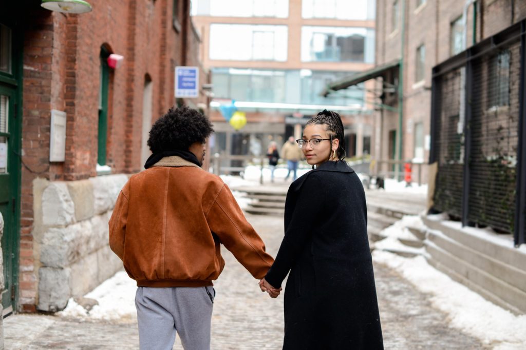 couple holding hands with woman looking backwards at camera at engagement photography session