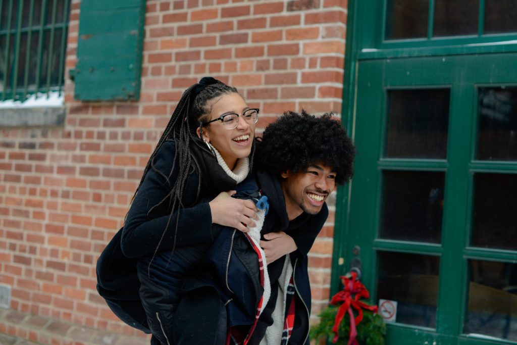 man giving laughing woman a piggyback ride at engagement photoshoot