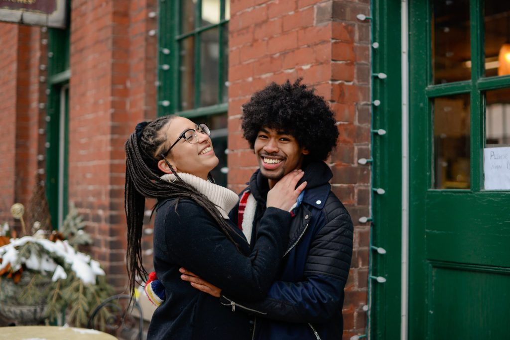 laughing couple against brick wall and green door for engagement photoshoot