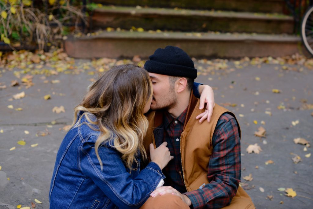 couple kissing outside surrounded by autumn leaves at engagement photography session