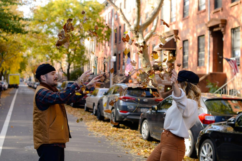 couple throwing up leaves outside in New York City streets at engagement photoshoot