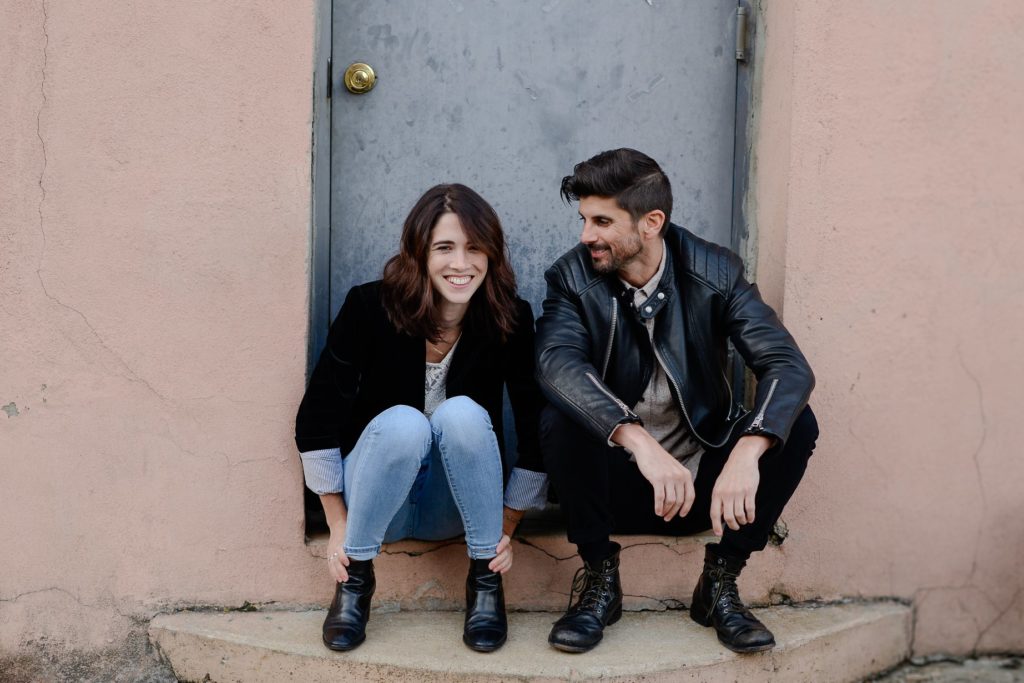 smiling couple seated in doorway posing for engagement photoshoot