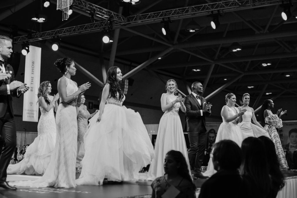 black and white photo of several models in wedding dresses on stage at Canada's Bridal Show 2019