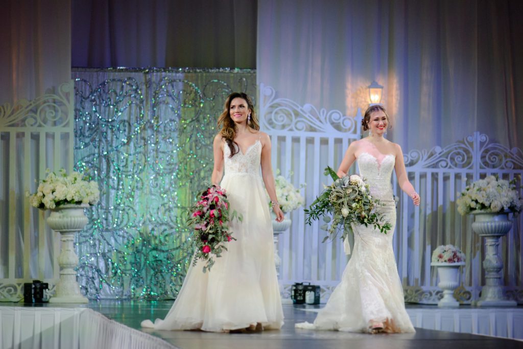 two models in wedding dresses with pink and white bouquets on runway at Canada's Bridal Show 2019